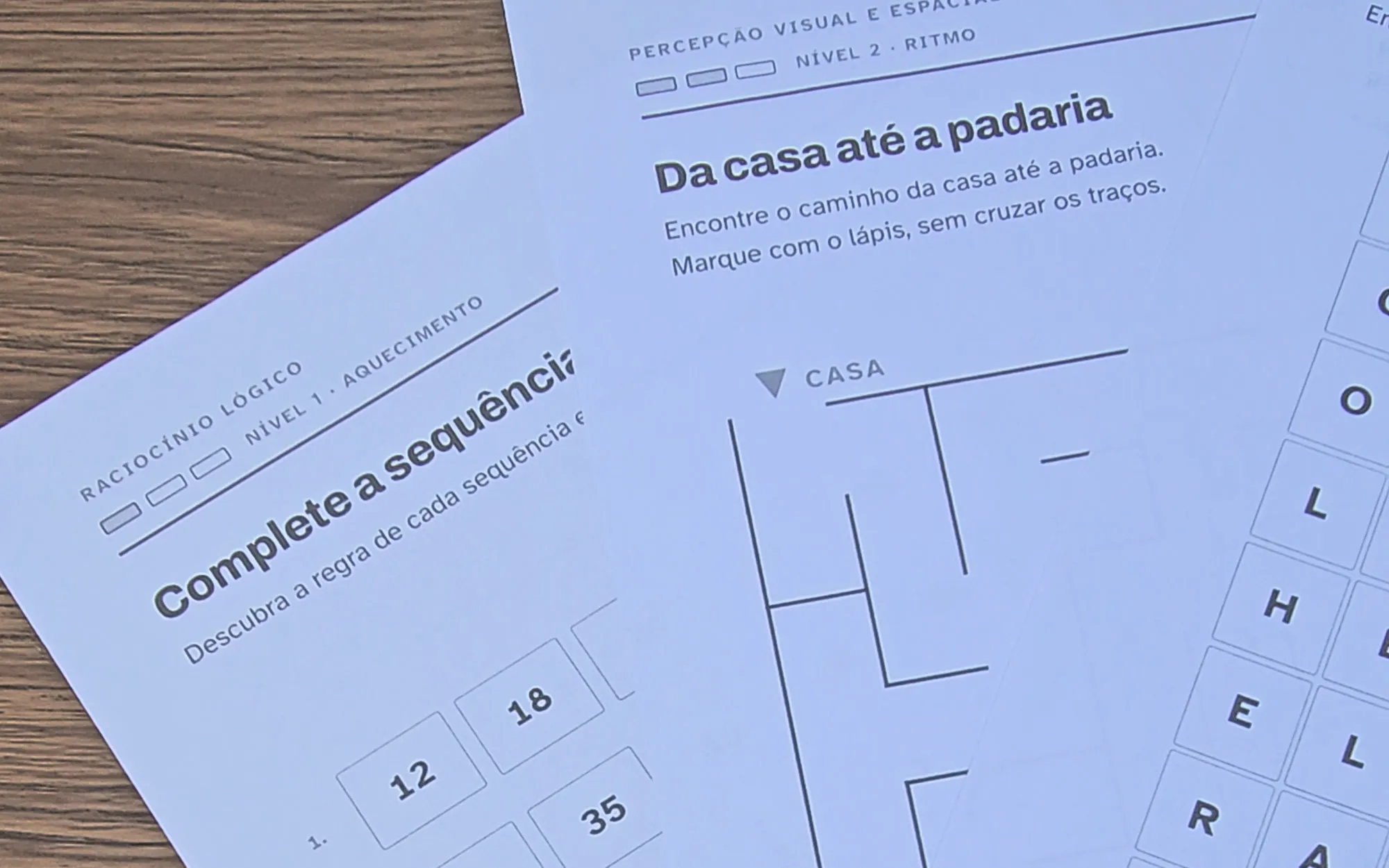 Folhas do kit sobrepostas sobre a mesa: sequências numéricas, labirinto e caça-palavras