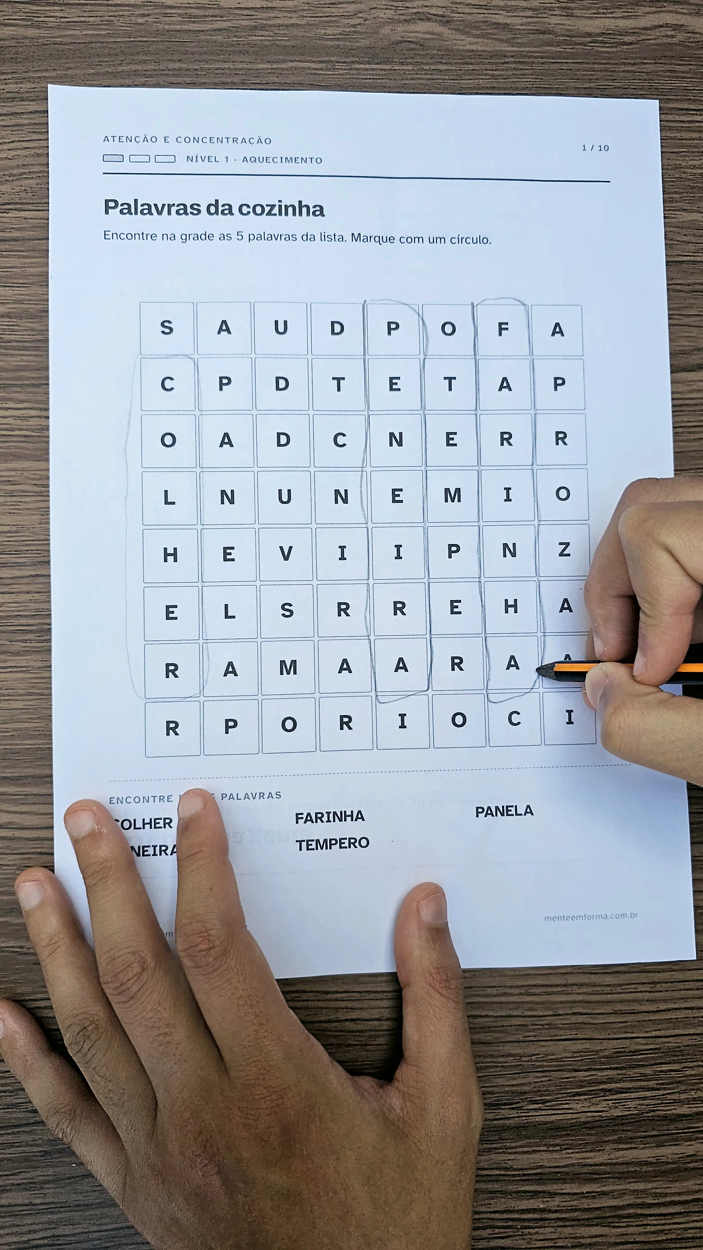 Duas mãos sobre uma folha de caça-palavras impressa, uma segurando o papel e a outra circulando uma palavra com lápis